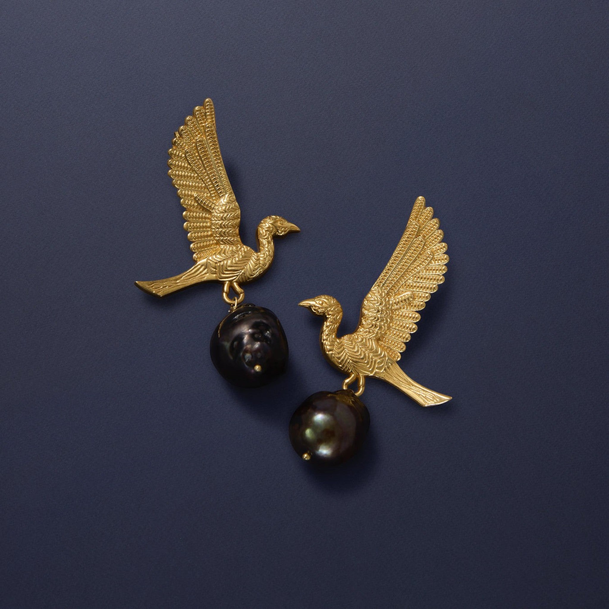 Tania Claire Australia gold-tone earrings with winged bird motif holding black baroque pearls.